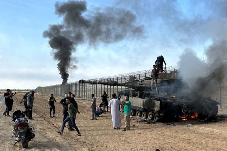 Người Palestine chụp ảnh bên cạnh chiếc xe tăng bốc cháy của Israel, sau khi chiếc xe bị các tay súng Hamas tấn công tại khu vực gần biên giới Israel - Gaza, ngày 7-10 - Ảnh: REUTERS