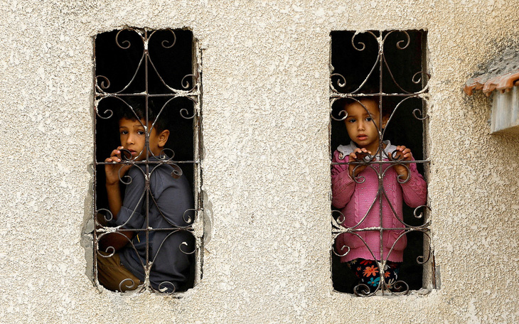 Hai đứa trẻ Palestine nhìn ra bên ngoài cửa sổ tại khu vực nhà ở bị Israel không kích ở thành phố KhanYounis, phía nam Dải Gaza, vào ngày 9-11 - Ảnh: Reuters