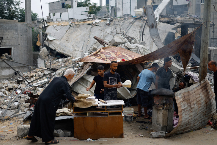 Người Palestine chuẩn bị thức ăn bên cạnh đống đổ nát của các tòa nhà tại Khan Younis, miền nam Gaza, ngày 13-11 - Ảnh: REUTERS