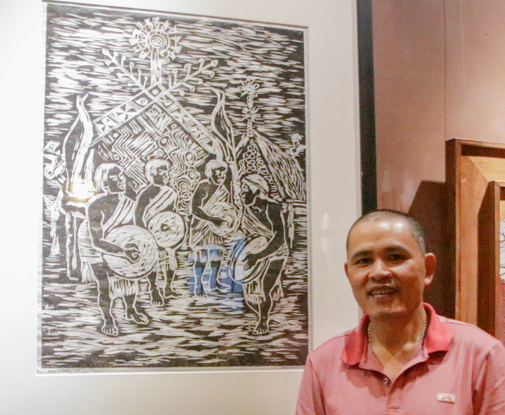 Họa sĩ Trương Văn Linh chụp cùng tranh khắc gỗ đen - trắng “Ngày hội bỏ mả 2” - Ảnh: HỒ LAM