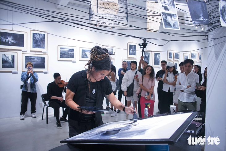 Nghệ sĩ Nicolás López trình diễn kỹ thuật vẽ màu nước trên giấy giang tại triển lãm &quot;Ngôn ngữ của nước&quot;. Anh đứng dưới tác phẩm sắp đặt lấy cảm hứng từ những cột điện hiện diện khắp Việt Nam - Ảnh: H.VY