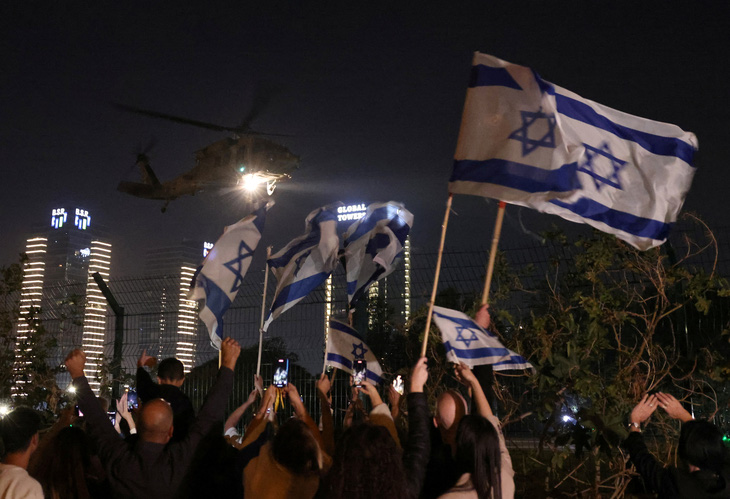 Người dân vẫy cờ Israel khi một chiếc trực thăng chở con tin được thả đến Petah Tikva, Israel, ngày 24-11 - Ảnh: REUTERS