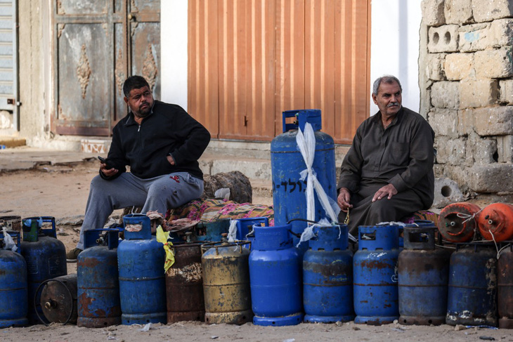 Người dân Palestine ngồi chờ bơm đầy các bình gas để nấu ăn ở gần cửa khẩu Rafah, ngày 25-11. Xe tải chở viện trợ, bao gồm nhiên liệu, thực phẩm và thuốc men, bắt đầu di chuyển vào Gaza qua cửa khẩu Rafah từ Ai Cập ngay sau khi lệnh ngừng bắn có hiệu lực từ sáng 24-11 - Ảnh: AFP