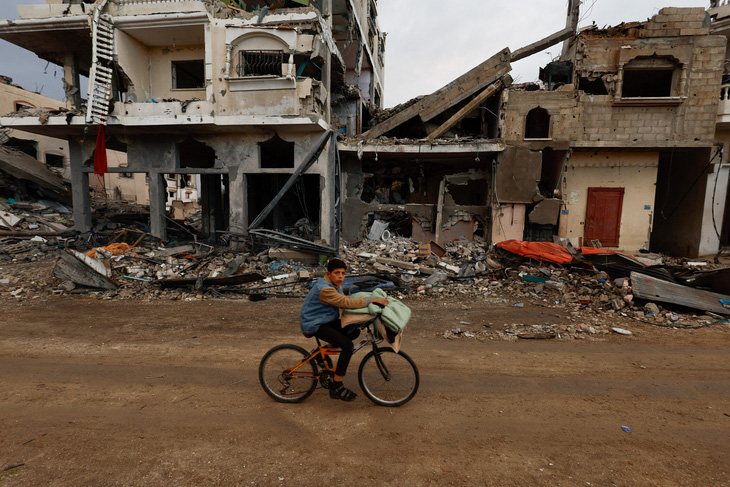 Một cậu bé Palestine đạp xe ngang qua những tòa nhà đổ nát ở Khan Younis, phía nam Gaza ngày 27-11 - Ảnh: REUTERS