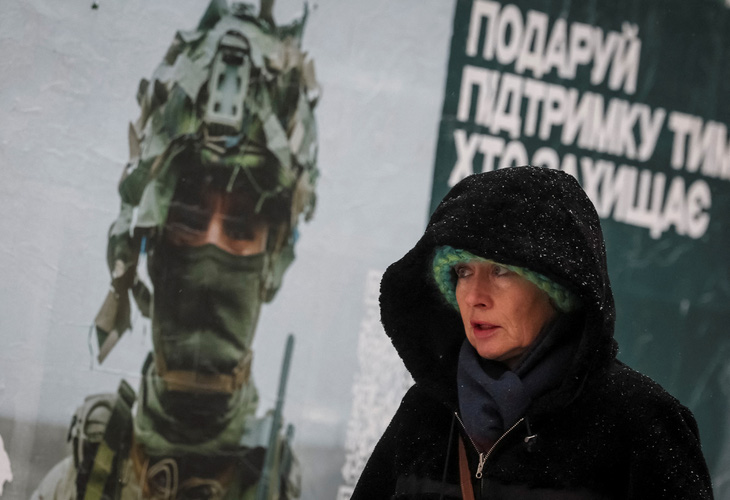 Một người phụ nữ đi ngang qua tấm áp phích quảng cáo có hình một quân nhân Ukraine trong trận tuyết rơi ở Kiev, Ukraine ngày 27-11 - Ảnh: REUTERS