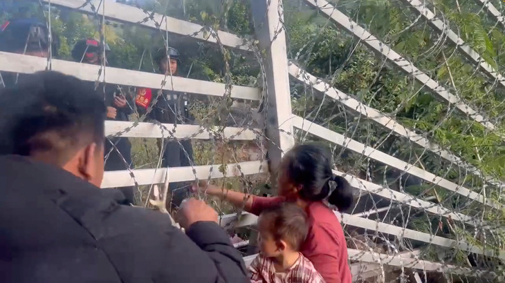 Một người phụ nữ có con ở phía Myanmar nói chuyện với cảnh sát Trung Quốc qua hàng rào biên giới. Đây là ảnh chụp màn hình video trên mạng xã hội quay ở thị trấn Laukkang, bang Shan, Myanmar và được đăng hôm 26-11 - Ảnh: REUTERS