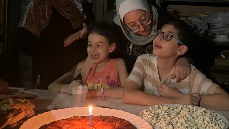 Cậu bé Hashem (bìa phải) đón sinh nhật 12 tuổi bên chiếc bánh dứa yêu thích, cùng với em gái Basma và mẹ Hiba - Ảnh: CNN