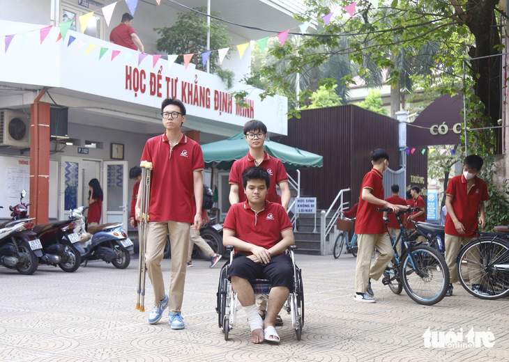 Nam sinh Trần Đại Phong đi xe lăn đến trường, được bạn bè hỗ trợ đưa vào lớp học - Ảnh: DANH TRỌNG