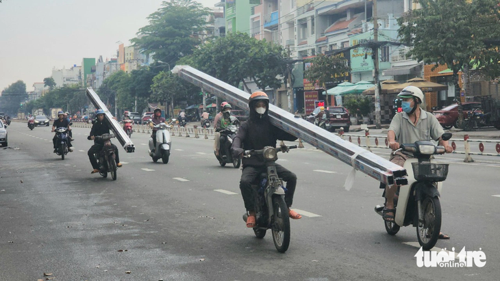 Hai người đi trên hai xe máy chở nhiều thanh kim loại dài ngoằng trên đường Tên Lửa (quận Bình Tân), chiều 7-11. Hai người này phải chạy một tay vì tay còn lại phải giữ thanh kim loại - Ảnh: NGỌC KHẢI