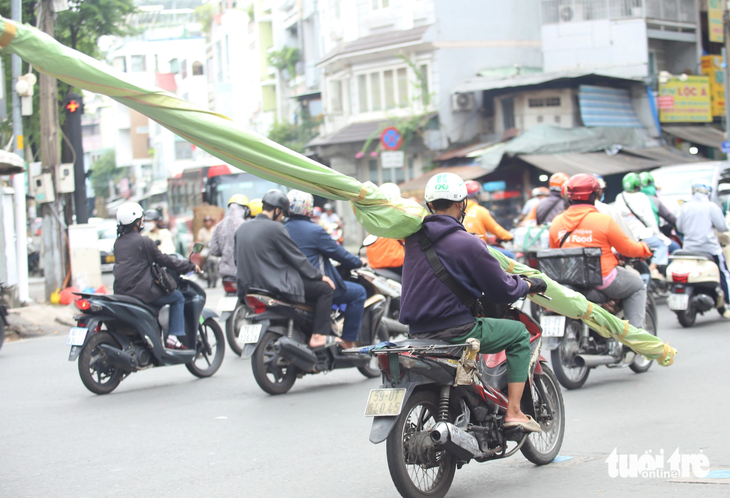 Nam thanh niên chạy xe máy bằng một tay, tay còn lại giữ một vật dài đang vác trên vai, chạy trên đường Ngô Gia Tự, quận 5 - Ảnh: MINH HÒA