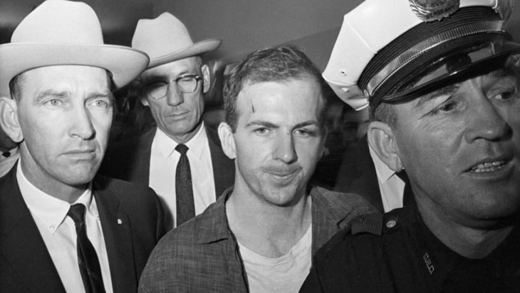 Lee Harvey Oswald (ở giữa, không đội mũ) bị bắt ở Dallas, bang Texas sau khi ám sát Tổng thống Mỹ John F. Kennedy vào ngày 22-11-1963 - Ảnh chụp màn hình RT/GETTY IMAGES