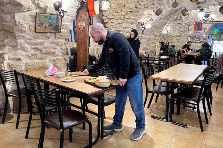 Người đồng sở hữu thế hệ thứ tư của nhà hàng Afteem, Ala'a Salameh, 42 tuổi, đặt thức ăn lên bàn bên trong nhà hàng ở Bethlehem - Ảnh: REUTERS