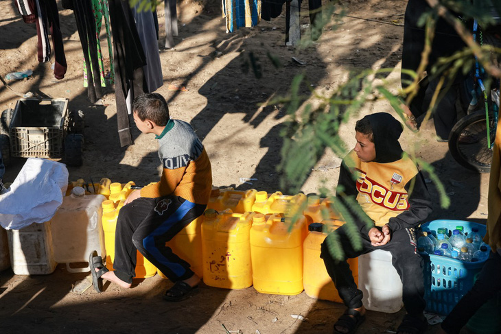 Một số trẻ em ngồi đợi lấy nước sạch tại một trạm cung cấp nước ở thành phố Rafah, miền nam Dải Gaza - Ảnh: AFP
