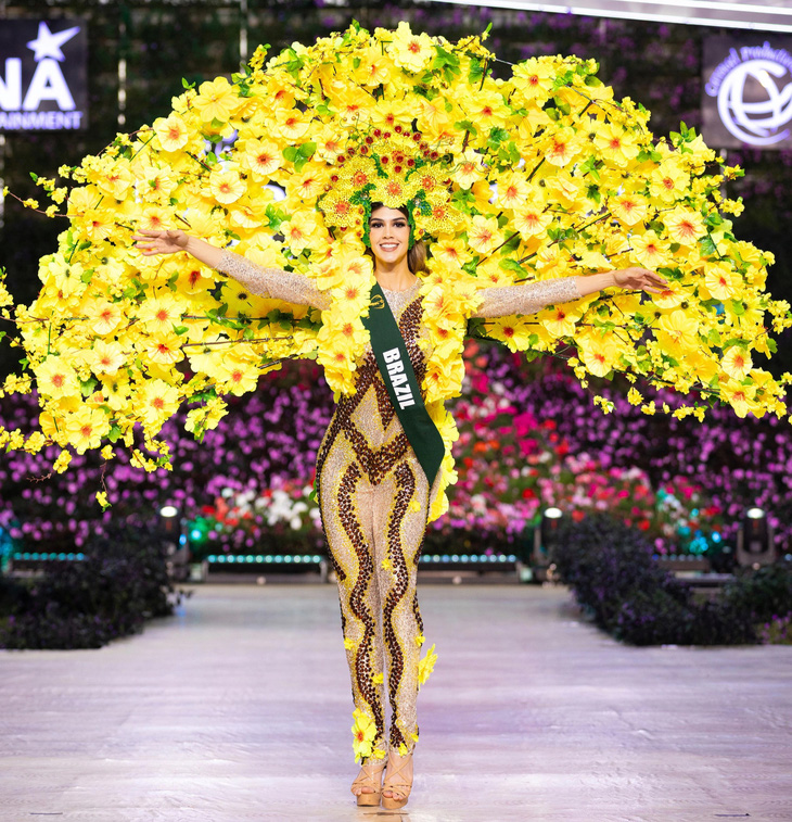 Bộ trang phục của người đẹp Brazil được lấy cảm hứng từ cây brazilwood - một loài cây có nguồn gốc từ rừng nhiệt đới Brazil. Cây có vảy và hoa màu vàng, bị đe dọa tuyệt chủng. Thiết kế này được làm bằng vật liệu tái chế, nhựa và giấy nghệ thuật. Hoa, lá và các đường màu nâu tượng trưng cho thân cây được vẽ bằng tay. Thiết kế hướng đến thông điệp bảo tồn thiên nhiên - Ảnh: BTC