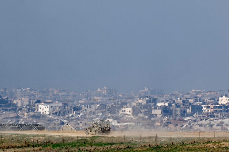 Ảnh chụp từ miền nam Israel cho thấy một chiếc xe quân sự của Israel di chuyển gần các tòa nhà bị hư hại ở Dải Gaza vào ngày 19-12 - Ảnh: REUTERS