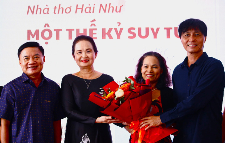 Nhà văn Bích Ngân (thứ hai từ trái qua) trao hoa cho con trai của nhà thơ Hải Như tại buổi tọa đàm Nhà thơ Hải Như, một thế kỷ suy tư - Ảnh: Hồ Lam