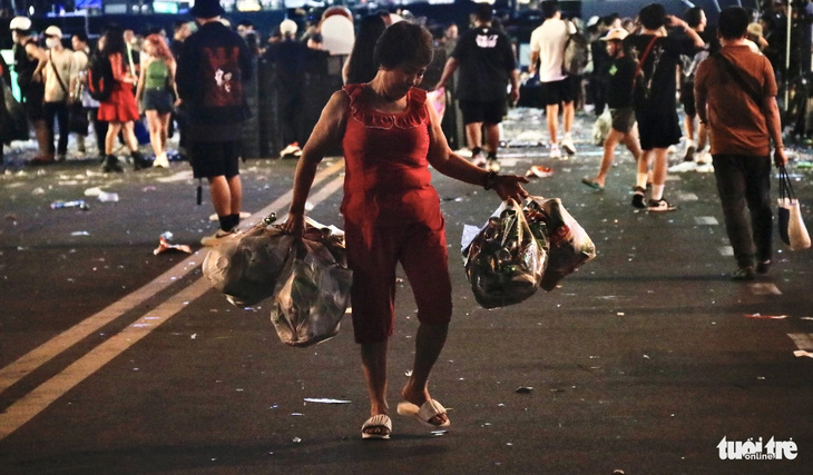 Người phụ nữ xách nhiều túi đựng chai nhựa nhặt tại phố đi bộ do người dân vứt lại - Ảnh: TIẾN QUỐC