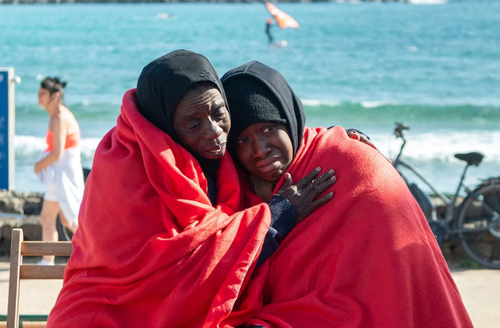 Hai di dân này đang ngồi nghỉ tạm trên bãi biển ở thị trấn Teguise, Tây Ban Nha sau khi đi bằng thuyền tới đây trong một đoàn có 48 người. (Adriel Perdomo/EPA)