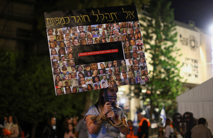 Một người  biểu tình cầm tấm biển in hình các con tin bị Hamas bắt cóc ở Tel Aviv, Israel, ngày 2-12 - Ảnh: REUTERS
