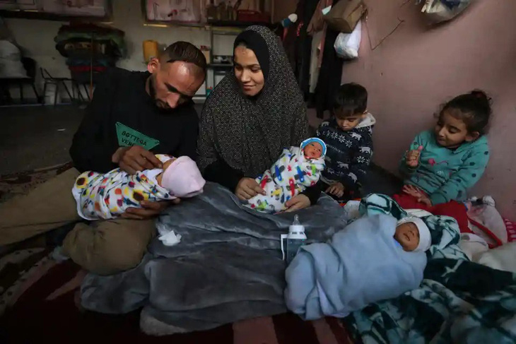 Vợ chồng anh Anmar và chị Iman al-Masri, những người Palestine phải rời bỏ nhà cửa để tránh bom đạn của Israel, đang ôm 3 trong 4 đứa con sinh tư tại một nơi trú ẩn trong trường học ở miền trung Dải Gaza hôm 28-12. Đứa trẻ còn lại đang được điều trị ở bệnh viện - Ảnh: AFP