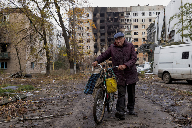 Người dân Ukraine đứng trước một dãy nhà hư hại do giao tranh tại Avdiivka - Ảnh: REUTERS