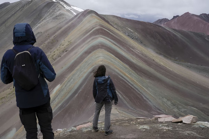 Các du khách đang đứng ngắm nhìn ngọn Núi cầu vồng đẹp như tranh vẽ ở Cusipata, Peru. Ngọn núi này vốn là nơi thu hút đông đảo du khách quốc tế nhưng gần đây tạm thưa vắng vì những bất ổn chính trị ở quốc gia Nam Mỹ - Ảnh: AP