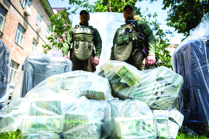 Hai thành viên Cơ quan chống tham nhũng quốc gia Ukraine đứng bên túi nhựa đựng đầy đô la Mỹ - tang chứng trong một vụ truy quét tham nhũng năm 2020. Ảnh: Reuters