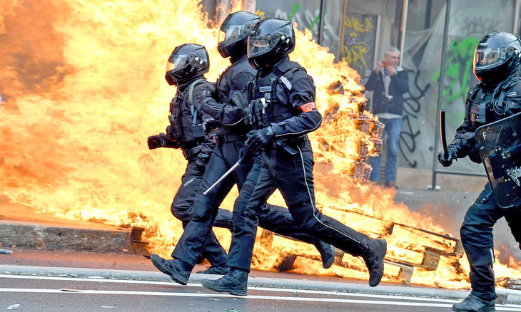 Cảnh sát chống bạo động chạy ngang qua một đám cháy khi đông đảo người biểu tình phản đối luật cải cách hưu trí ở Paris, Pháp hôm 23-3 - Ảnh: AFP