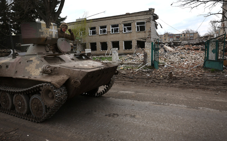 Quân nhân Ukraine lái thiết giáp ngang qua ngôi trường bị phá hủy trên đường tới thành phố tiền tuyến Bakhmut hôm 11-4 - Ảnh: REUTERS