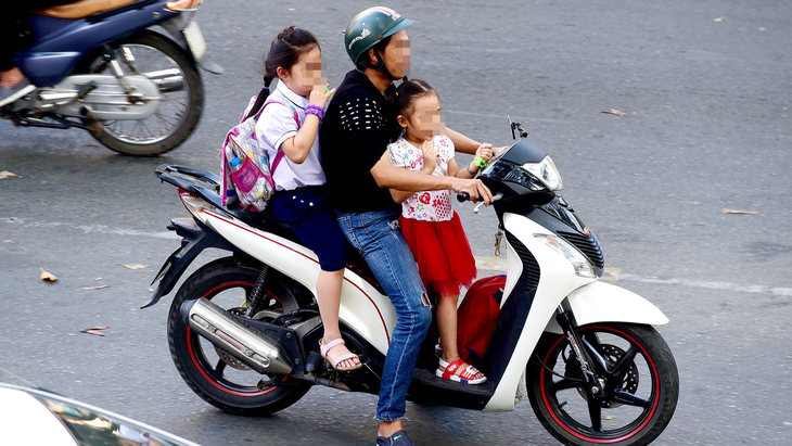 Tình trạng để trẻ ngồi và đứng trước xe máy, không đội mũ bảo hiểm rất phổ biến và rất nguy hiểm - Ảnh: QUANG ĐỊNH