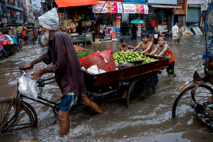 Đám trẻ con cùng hợp sức đẩy xe bán trái cây của ông lão trên một con đường ngập lụt do mưa lớn ở thủ đô Dhaka (Bangladesh) vào ngày 12-6. Ảnh: Reuters