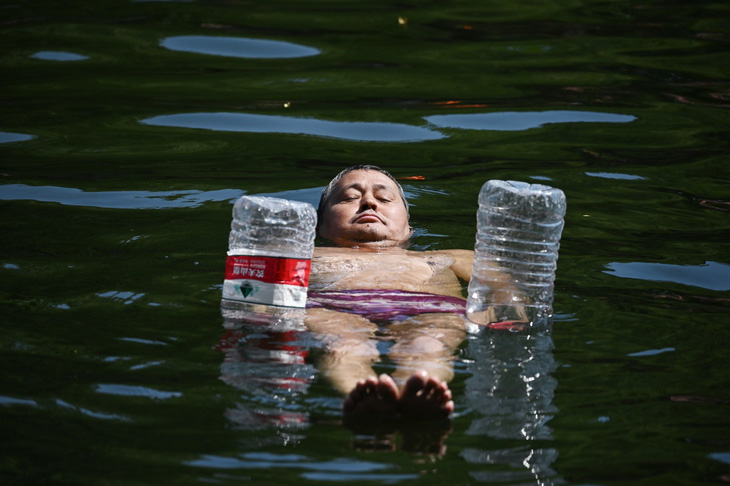 Người đàn ông sử dụng hai chai nhựa rỗng để làm phao trong lúc giải nhiệt trên một con kênh ở Bắc Kinh, ngày 22-6. Dữ liệu cho thấy thủ đô Trung Quốc những ngày qua có lúc nhiệt độ chạm ngưỡng 40 độ C, cao nhất trong nhiều năm trở lại đây - Ảnh: AFP
