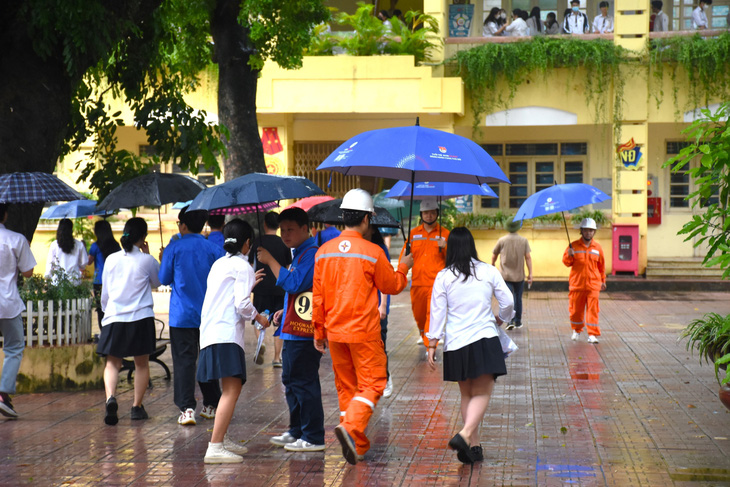 Những tình nguyện viên áo cam sẵn sàng hỗ trợ thí sinh di chuyển vào trường dưới cơn mưa