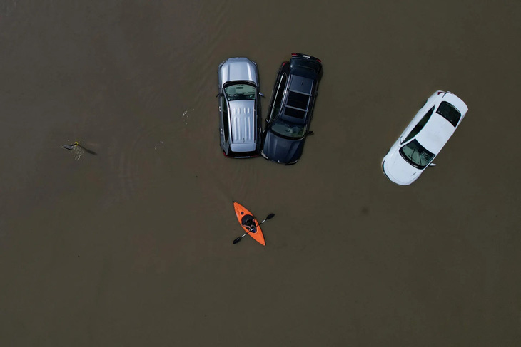 Một người ngồi trên chiếc xuồng phao đang chèo qua mấy chiếc xe hơi ngập trong nước lũ sau các trận mưa lớn gần đây tại Montpelier, thành phố thủ phủ tiểu bang Vermont, Mỹ (Brian Snyder/REUTERS)