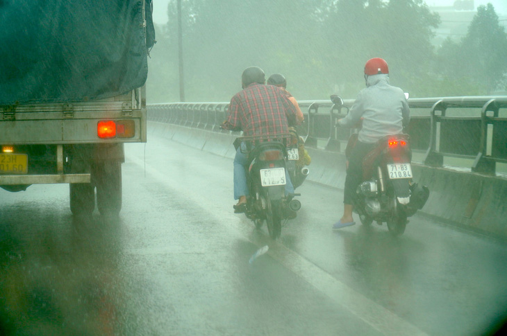 Một số người đi xe máy qua cầu Rạch Miễu gặp lúc mưa phải nép vào xe tải để tránh bị gió quật - Ảnh: MẬU TRƯỜNG