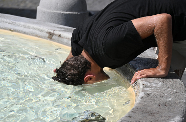 Người đàn ông ụp mặt xuống nước để làm mát ở một vòi nước tại thủ đô Rome (Ý) ngày 18-7. Nắng nóng cực đoan ở châu Âu do sóng nhiệt và cháy rừng là một trong chủ đề thời sự chính tuần này - Ảnh: AFP