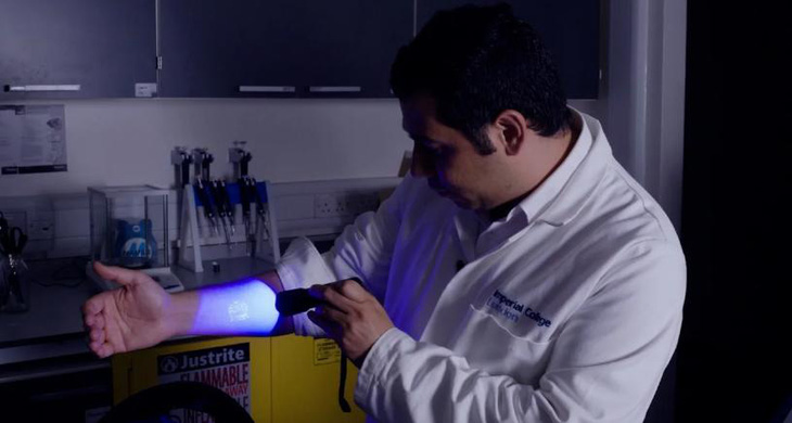 Tại phòng thí nghiệm của Đại học Hoàng gia London, Ali Yetisen trình diễn một con dấu trên cánh tay được tạo ra bằng mực xăm phát sáng dưới ánh sáng đèn pin - Ảnh: CNN