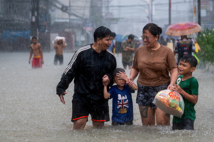 Một gia đình lội nước trong một khu vực ngập do mưa lớn và ảnh hưởng của bão Doksuri ở thành phố Balagtas, tỉnh Bulacan (Philippines) ngày 29-7 - Ảnh: REUTERS