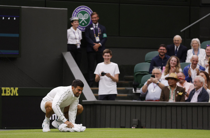 Djokovic khiến người hâm mộ khán đài cười rộ khi dùng khăn lau sân đấu - Ảnh: REUTERS