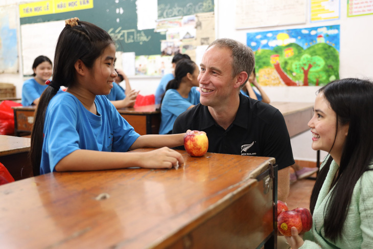 Ông James trao táo và trò chuyện với một học sinh lớp 5 tại Làng May Mắn - Ảnh: CẨM TIÊN