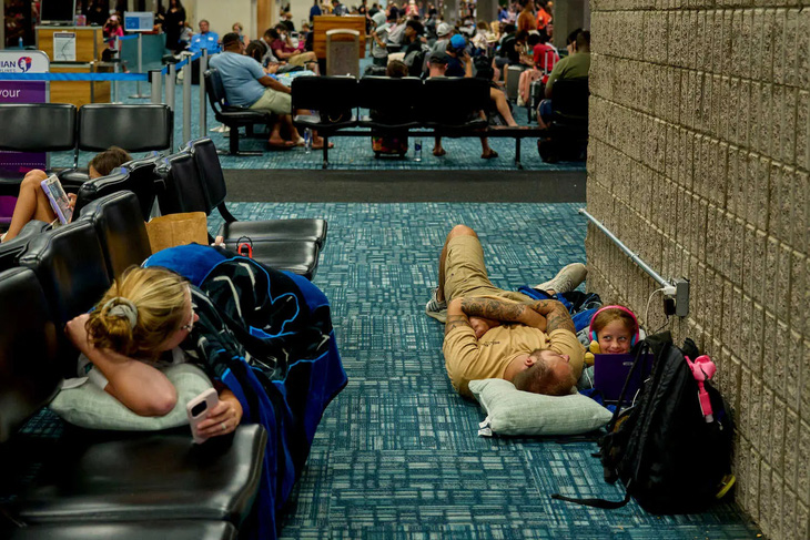 Những người bị kẹt tại sân bay phải tranh thủ thời gian luân phiên sử dụng ổ điện để sạc thiết bị điện tử - Ảnh: NEW YORK TIMES