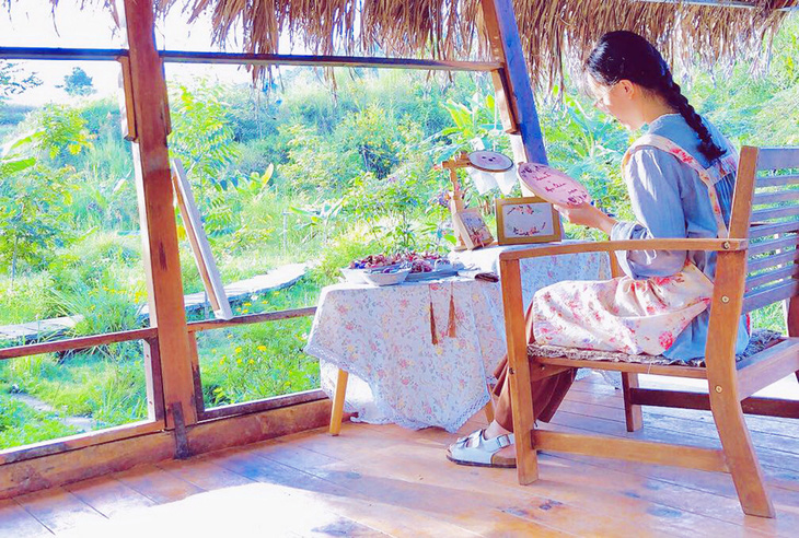 Thanh sitting in front of an embroidery frame, peaceful scene where the green garden is a great inspiration - photo: Ha Thanh