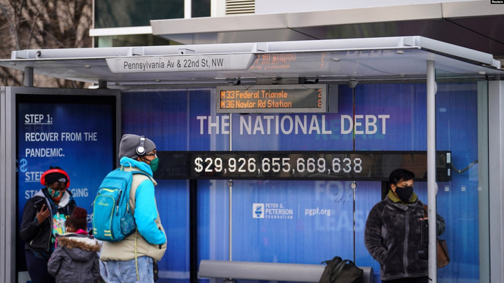 Người dân đeo khẩu trang đứng chờ ở một trạm dừng xe buýt có hiển thị số nợ công của nước Mỹ trong dịch COVID-19 vào ngày 31-1-2022 ở Washington (Mỹ) - Ảnh: Reuters