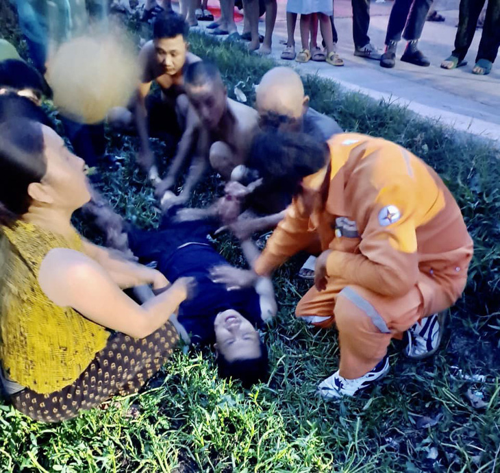 Anh Nguyễn Tuấn Vũ (người nằm) sau khi đưa được người bị nạn lên bờ thì anh cũng kiệt sức. Trong ảnh là cảnh người dân và các đồng nghiệp đang tìm cách chăm sóc anh trước khi đưa vào bệnh viên cấp cứu -  Ảnh: HƯƠNG NGUYÊN