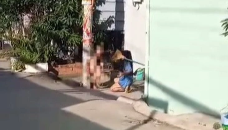 Người phụ nữ dùng chổi đánh bé trai trần truồng đang bị trói vào cột điện - Ảnh cắt từ video do người dân ghi lại