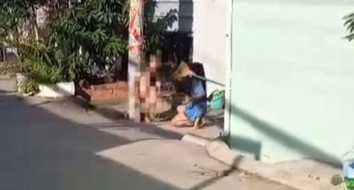 Bé trai trần truồng bị trói vào cột điện và bị người phụ nữ dùng chổi đánh - Ảnh cắt từ video do người dân ghi lại