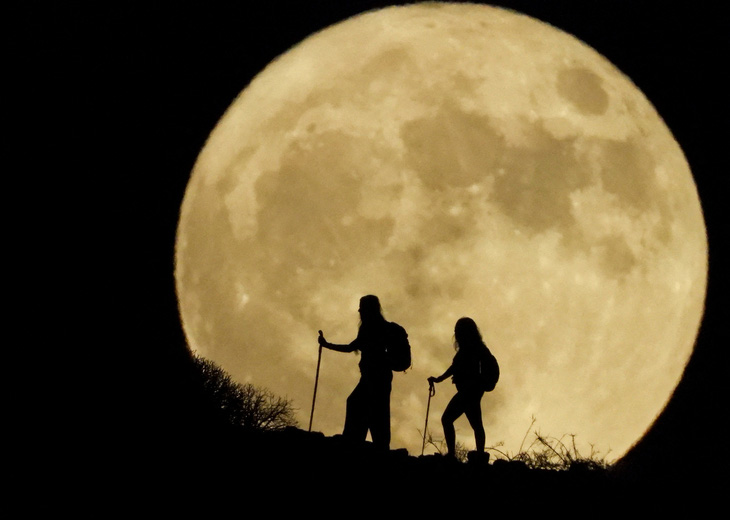 Hai người phụ nữ đang leo núi, ở phần nền phía xa họ là mặt trăng tròn giữa tháng, cũng chính là hiện tượng siêu trăng có tên là “Trăng Cá tầm”. Góc ảnh thú vị trên được ghi lại ở khu Arguineguin trên đảo Gran Canaria của Tây Ban Nha vào ngày 1-8-2023 - Ảnh: REUTERS