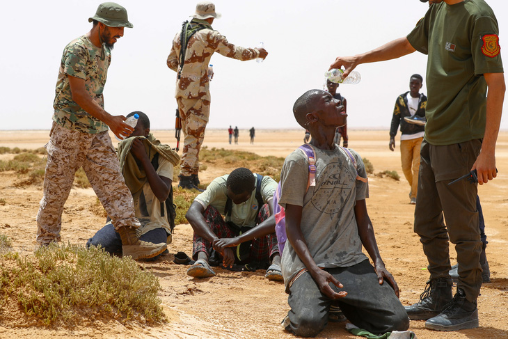Lực lượng an ninh biên giới Libya cung cấp nước cho những người nhập cư từ châu Phi hôm 31-7. Những người này được cho là bị chính quyền Tunisia bỏ rơi sau khi họ đến một khu vực gần biên giới Libya - Tunisia - Ảnh: AFP