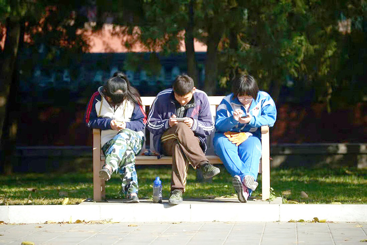 Nhóm người trẻ Trung Quốc chăm chú bấm điện thoại di động trên băng ghế tại công viên ở thủ đô Bắc Kinh (Trung Quốc) - Ảnh: AFP
