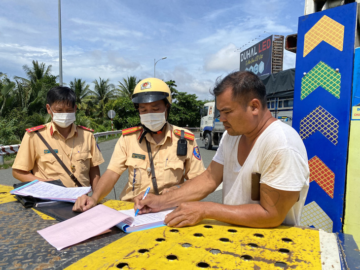 Một tài xế bị cảnh sát giao thông lập biên bản xử phạt do chạy xe qua cầu Rạch Miễu vào khung giờ cấm - Ảnh: MẬU TRƯỜNG